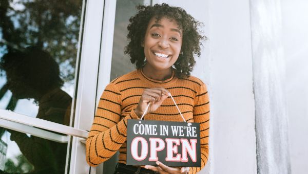 Black woman business owner holding open sign and smiling